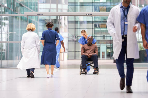 infermiera donna che indossa scrub che ruota paziente in sedia a rotelle attraverso la hall del moderno edificio ospedaliero - grandangolo tecnica fotografica foto e immagini stock