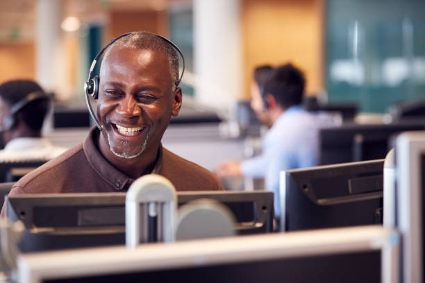 mature businessman wearing telephone headset talking to caller in customer services department - call center imagens e fotografias de stock