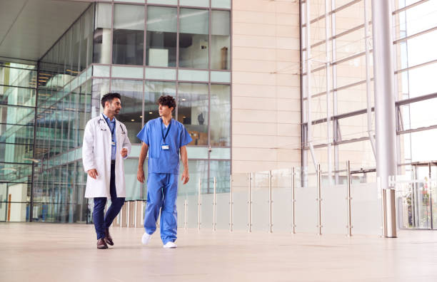 personnel médical masculin parlant pendant qu'ils marchent par le hall du bâtiment moderne d'hôpital - grand angle photos et images de collection