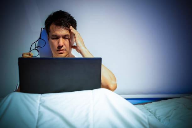 istock headache, tense young asian man working on laptop computer in bed at night 1190167708