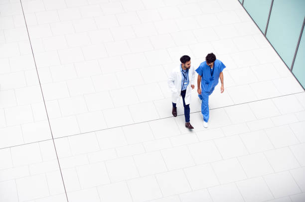 Overhead View Of Medical Staff Talking As They Walk Through Lobby Of Modern Hospital Building Overhead View Of Medical Staff Talking As They Walk Through Lobby Of Modern Hospital Building wide angle stock pictures, royalty-free photos & images