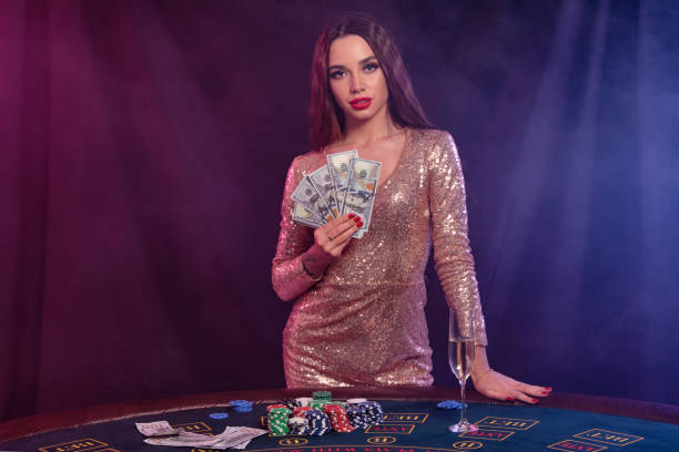 dziewczyna gra w pokera w kasynie, trzymając pieniądze. pozowanie przy stole z frytkami, szampanem, gotówką na nim. czarny, tło dymu. zbliżenie - casino black and white gambling chip gambling zdjęcia i obrazy z banku zdjęć