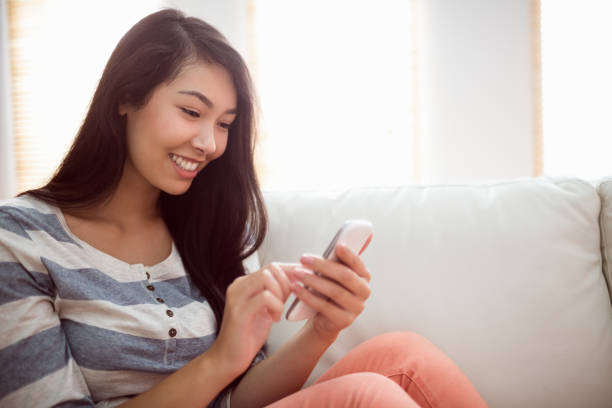 istock Smiling asian woman on couch using phone 1190168757