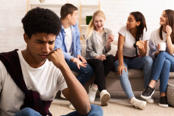 istock Upset bullied guy sitting alone, excluded by bad friends 1190169091
