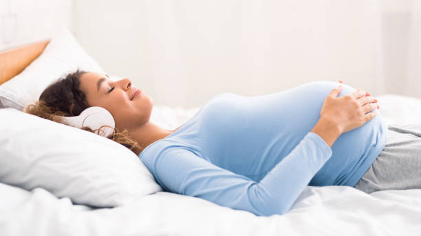 femme enceinte détendue appréciant la musique dans des écouteurs - lying on side audio photos et images de collection