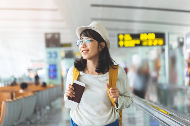 la donna asiatica indossa occhiali, il cappello con lo zaino giallo è in possesso di biglietto volante, passaporto nella sala dell'aeroporto. - airport airplane travel airport lounge foto e immagini stock