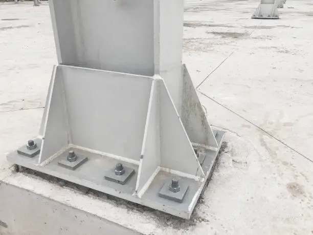 Metal pillar fastened to basement with anchor bolts and nuts. Supporting structures, metal frame of prefabricared building