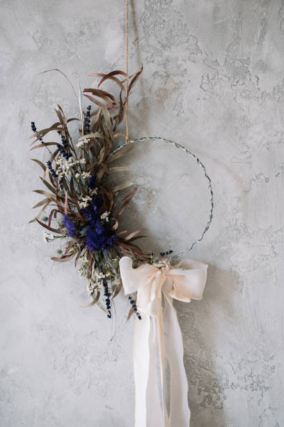 Beautiful hand made everlasting dry wreath made of dry flowers, eucalyptus tied with tender pastel coloured bow on the grey wall background stock photo