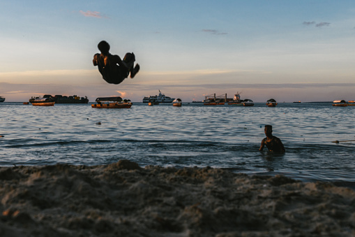 Zanzibar, Tanzania - February 21, 2019: african boys jumping flip over at Zanzibar beach at sunset