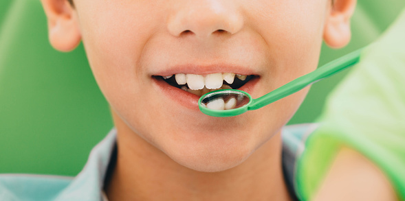 cropped child's smile while dental exam with dental mirror