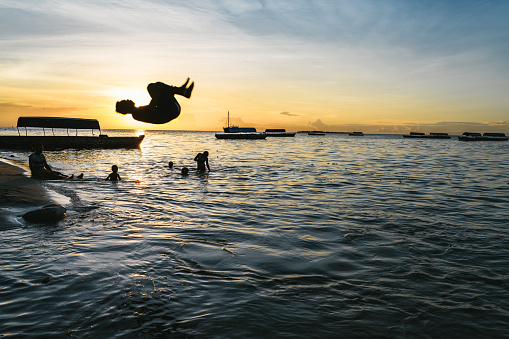 Zanzibar, Tanzania - February 21, 2019: african boys jumping flip over at Zanzibar beach at sunset