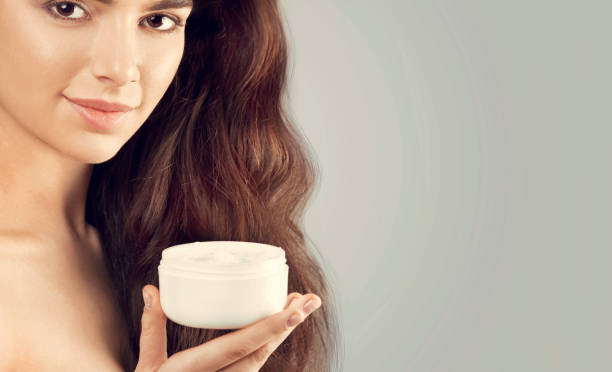 Skincare. Beauty Concept. Young pretty woman holding cosmetic cream. Soft skin and naked shoulders,model with light nude make-up, portrait of female holding moisturizing cream in her hand. Skin Protection and dermatology. Skincare. Beauty Concept. Young pretty woman holding cosmetic cream. Soft skin and naked shoulders,model with light nude make-up, portrait of female holding moisturizing cream in her hand. Skin Protection and dermatology. Best Hair Mask for Frizzy Hair stock pictures, royalty-free photos & images