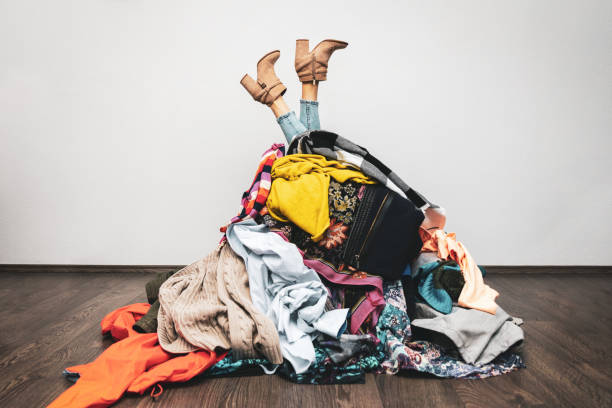 woman legs out of a pile of clothes on the floor. shopping addiction concept - monte roupa imagens e fotografias de stock
