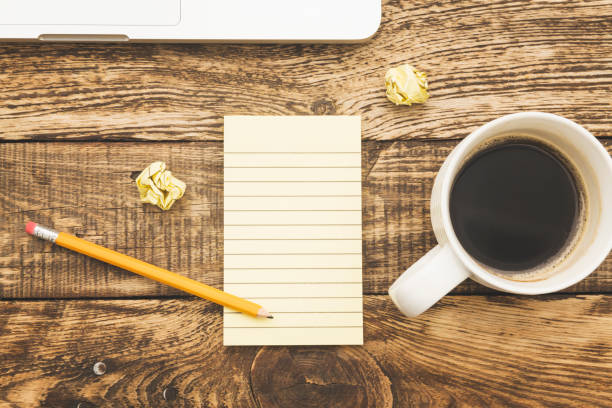 Studio shot of a creative work station on a rustic wooden desk. A blank notepad, a pencil, and a hot coffee drink,