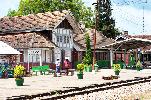 Kalaw railway station , Shan State, Myanmar. Passengers dressed in colourful but shabby working clothes standing together or walking  companionably on British colonial architecture Kalaw railway station platform showing the typical English building style with decoration alongside the railway line