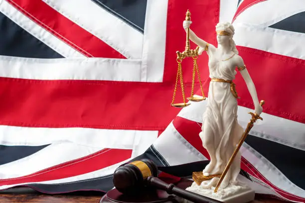 Social contract and the rule of law in the United Kingdom of Great Britain concept theme with statue of goddess Justice wooden gavel and the UK flag or the Union Jack in background with copy space