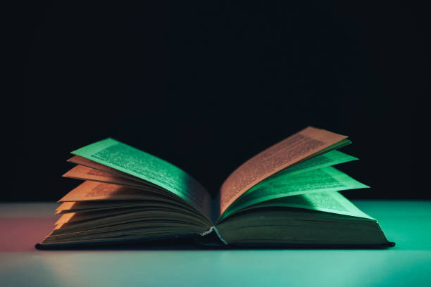 istock Beautiful open old book in the color light on a table and night background. 1190190334