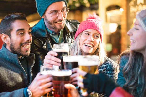 amis buvant de la bière au bar de brasserie en plein air sur l'heure d'hiver - concept d'amitié avec les jeunes ayant l'amusement ensemble griller à la promotion d'happy hour - foyer sur la fille avec le chapeau rose - filtre chaud de néon - apres ski photos photos et images de collection