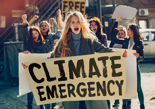 Young woman with poster in front of people protesting about climate changing on the street. Meeting about problem in ecology, environment, global warming, industrial influence, climate emergency.
