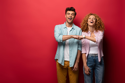 beautiful cheerful couple bumping fists, isolated on red