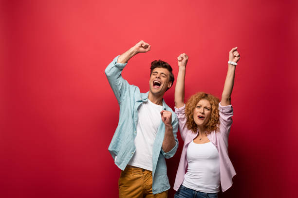 istock excited young couple celebrating triumph, isolated on red 1190200214