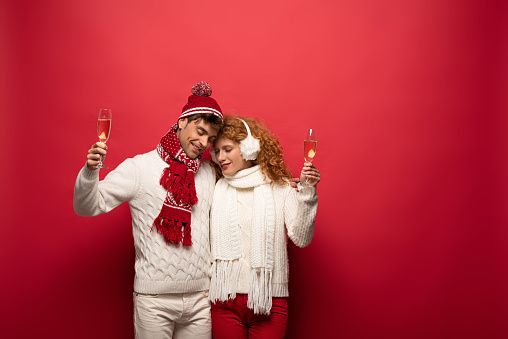 beautiful couple in winter outfit hugging and holding champagne glasses, on red
