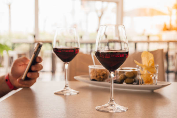 aperitivo con antipasto per due con 2 bicchieri di vino rosso - mano di un uomo distratto dai social sul suo smartphone (cellulare) - wine red red wine cocktail foto e immagini stock