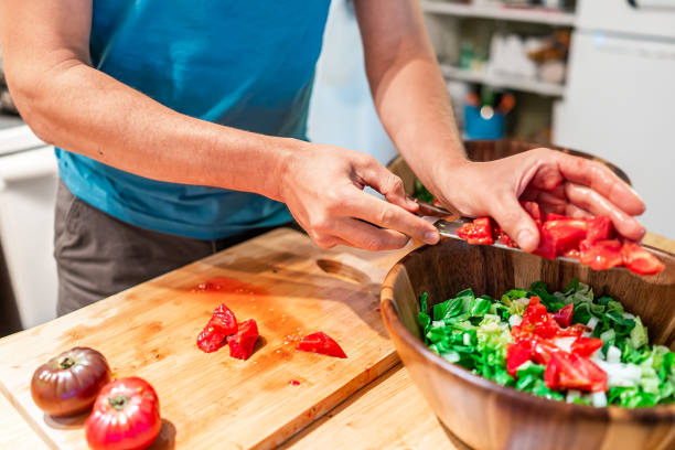 hombre cortando verduras en la mesa de la tabla de cortar en la cocina colocando jugosos tomates de reliquia roja con color vibrante de jardín en cuenco de madera ensalada - heirloom tomato tomato vegetable fruit fotografías e imágenes de stock