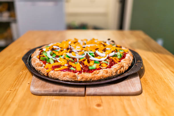 Homemade cooked pizza with tomato sauce and toppings green bell peppers onions chopped and melted orange vegan cheddar cheese on kitchen table