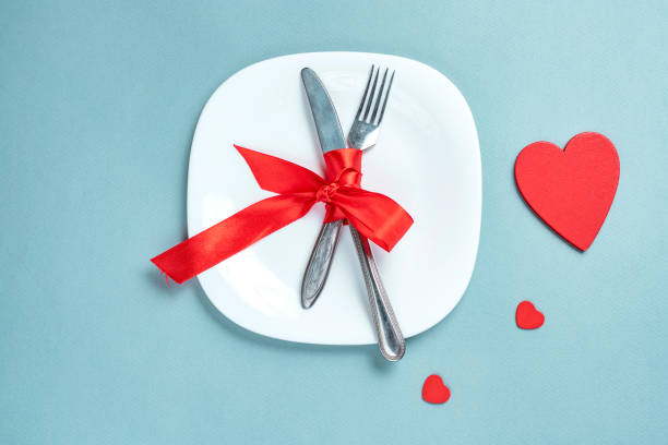 istock Valentine's day table setting with plate, fork, knife, gift box and red heart, on blue tablecloth background top view copy space. 1190224617