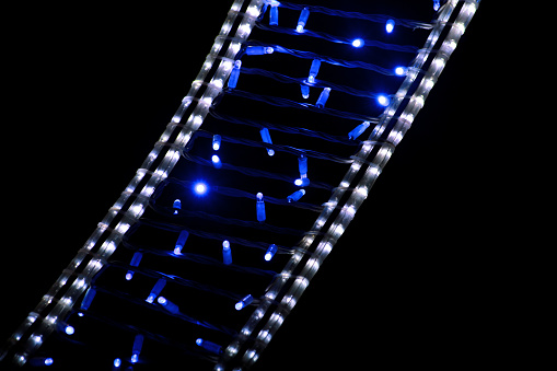 Part of Christmas decorative blue and white flashing lights, close up. Street detail of New Year and Christmas decorations, string rice lights bulbs. Ornaments to christmas celebration, holiday scene.
