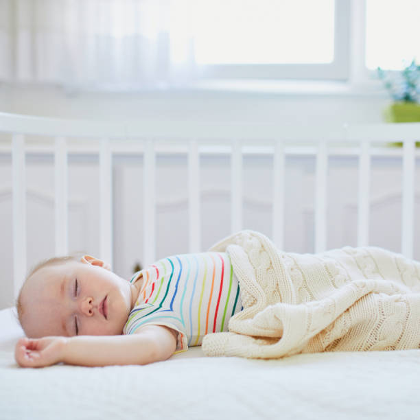 Baby sleeping in co-sleeper crib attached to parents' bed Adorable baby girl sleeping in co-sleeper crib attached to parents' bed. Little child having a day nap in cot. Sleep training concept. Infant kid in sunny nursery sidecar photos stock pictures, royalty-free photos & images