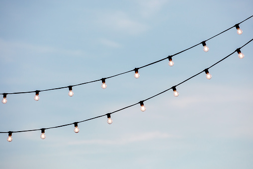 light bulbs garlands on a background of blue sky. Christmas lighting in the afternoon.
