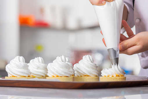 Female chef with confectionery bag squeezing cream on cupcakes.