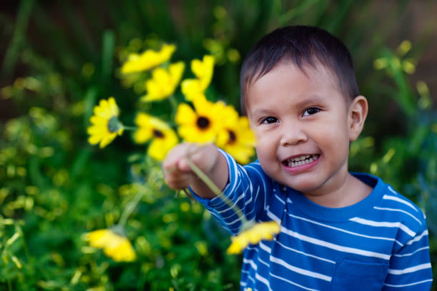 Smiling young son giving an arrangement of yellow flowers he is holding to show affection and love. stock photo