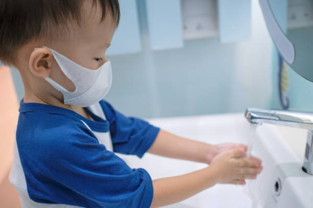 bambino asiatico di 3 - 4 anni che indossa una maschera medica protettiva lavandosi le mani sul lavandino in bagno pubblico / bagno per bambini - messa a fuoco morbida e selettiva - 2 3 years immagine foto e immagini stock