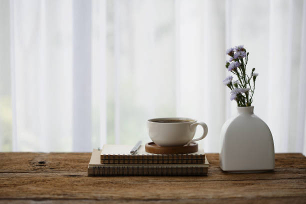 istock white coffee cup with diary notebook and flower in vase on wooden table on front of curtain 1190277355