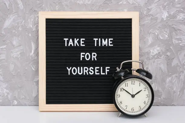 Take time for yourself. Motivational quote on letterboard and black alarm clock on table against stone wall. Concept inspirational quote of the day.