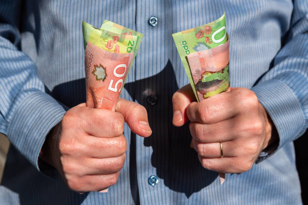 uomo che tiene saldamente banconote canadesi da venti e cinquanta dollari in entrambe le mani - banconota di dollaro canadese foto e immagini stock