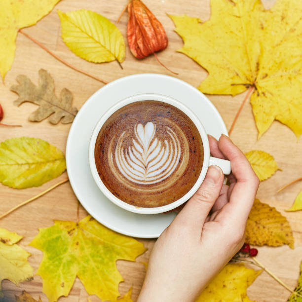 Autumn flat lay composition with dry leaves wreath frame and coffee latte cup in woman hand on wood background.