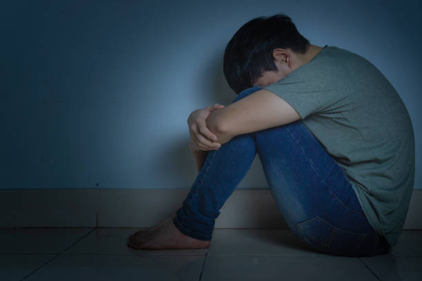 istock sad man hug his knee and cry sitting alone in a dark room. Depression, unhappy, stressed and anxiety disorder concept 1190307607