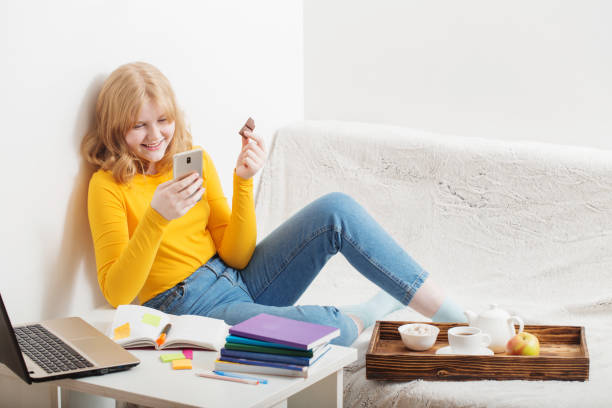 teen girl eating chocolate and looking at the mobile phone screen.  online education,e-learning. - homework teenager mobile phone school imagens e fotografias de stock