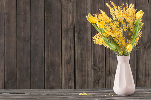 tulips and mimosa in vase on dark wooden background