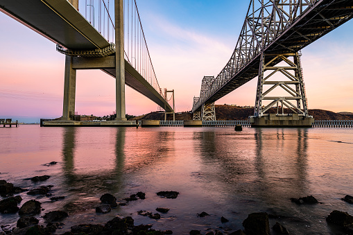 A vivid sunrise fills the sky on a crisp autumn morning, while reflections of the Carquinez Bridge provide a prominent subject in Crockett, California.