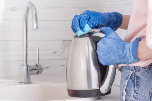 a residential cleaning service worker cleans an electric kettle.