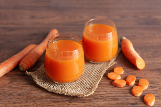succo di carota in un bicchiere e carote fresche su un tavolo. bevanda dietetica sana in un bicchiere su sfondo tavolo di legno. - healthy eating juice vegetable juice vegetable foto e immagini stock