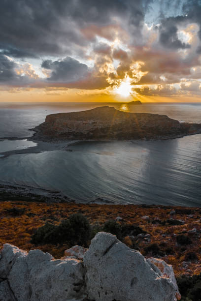 istock The sun sets in clouds behind a small island 1190333386
