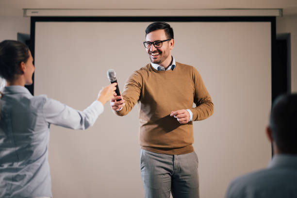 istock Smiling host presenting guest speaker on a seminar, giving microphone. 1190337742