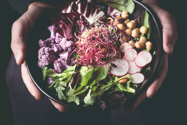 gesundes abendessen, mittagessen. mann essen vegane superbowl oder buddha schale mit gemüse, frischen salat, kichererbsen, sojasprossen, lila brokkoli - rohkosternährung stock-fotos und bilder