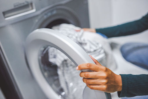 Closeup shot of an unrecognisable woman using a washing machine to do laundry at home